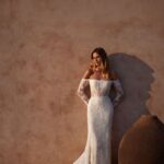 A woman in a white dress leaning against a wall