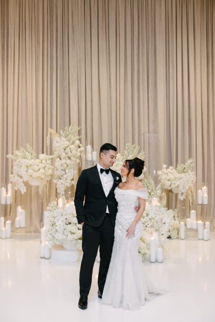 A couple standing in front of a white flower wall.