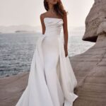 A woman in white dress standing on the side of a body of water.