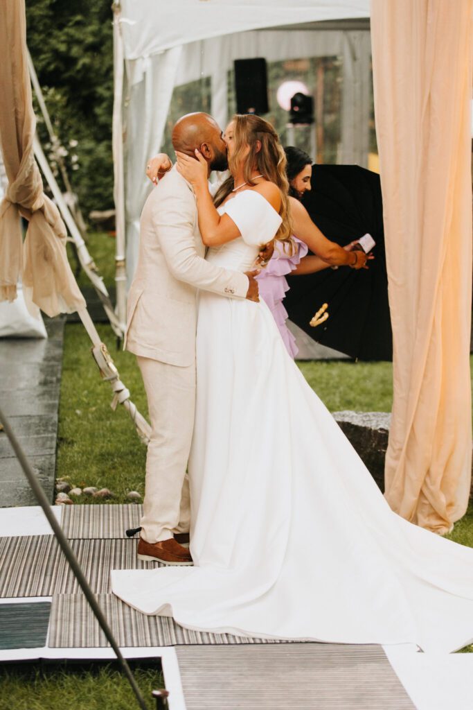 A man and woman kissing in front of an umbrella.
